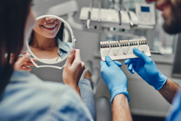 Woman at a dental clinic smiling in the mirror and the male dentist is sitting next to her holding the dental equipment