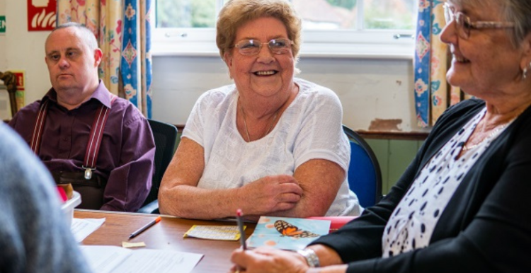 Two elderly ladies and a man sitting at a table and smiling.
