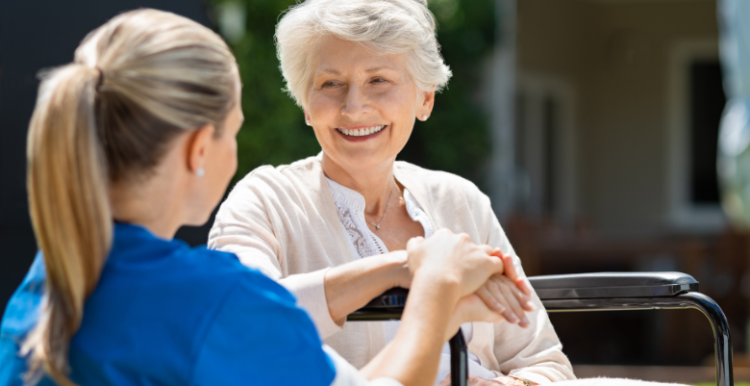 A nurse holding the hand of an elderly woman sitting on a wheelchair.