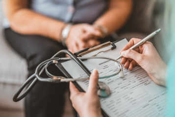 A healthcare professional writing information on a paper attached to a clip board.