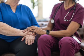 A hospice nurse in a purple uniform comforting an elderly person.