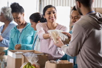 People volunteering at a food bank by handing out food.