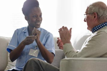 A female medical professional communicating with an elderly man through sign language.