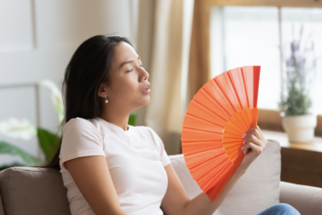 Asian woman waving fan cooling herself in hot weather indoors